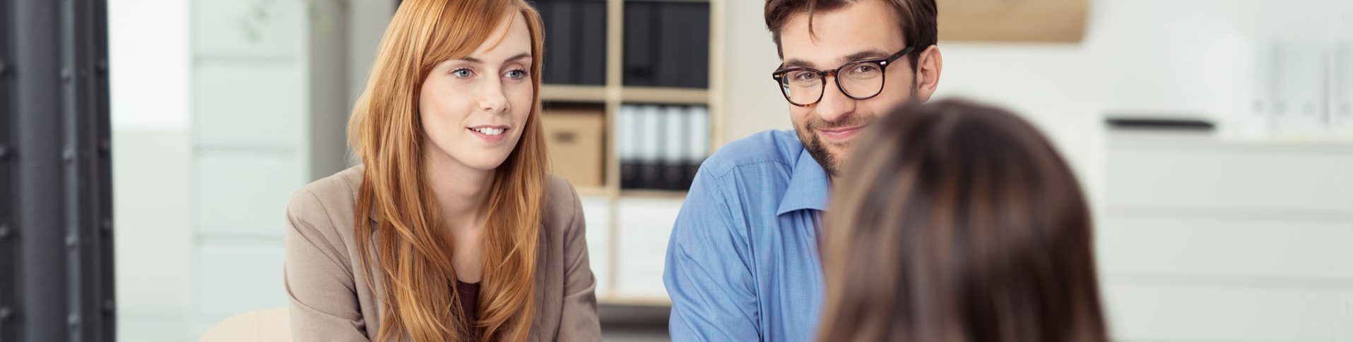 A young couple sits at a desk in front of a counsellor in financial recovery