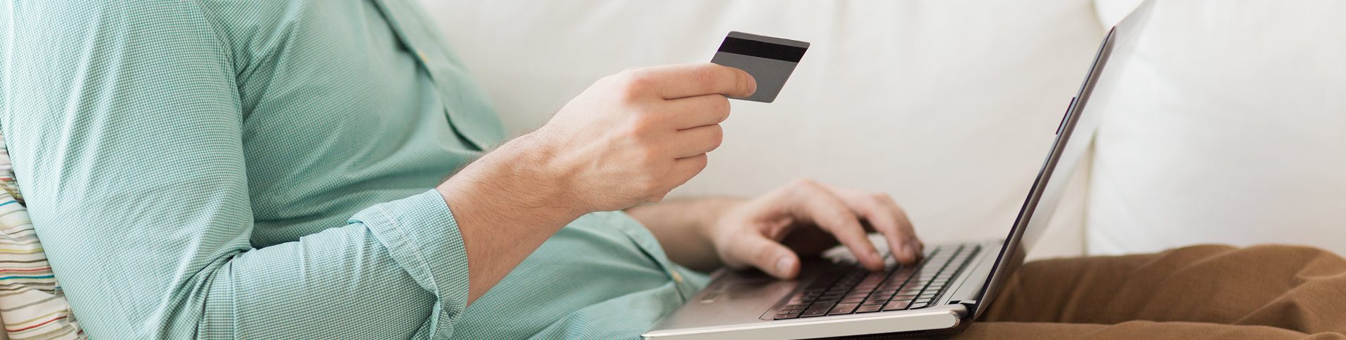 A man sitting on a couch makes a credit card payment on a computer